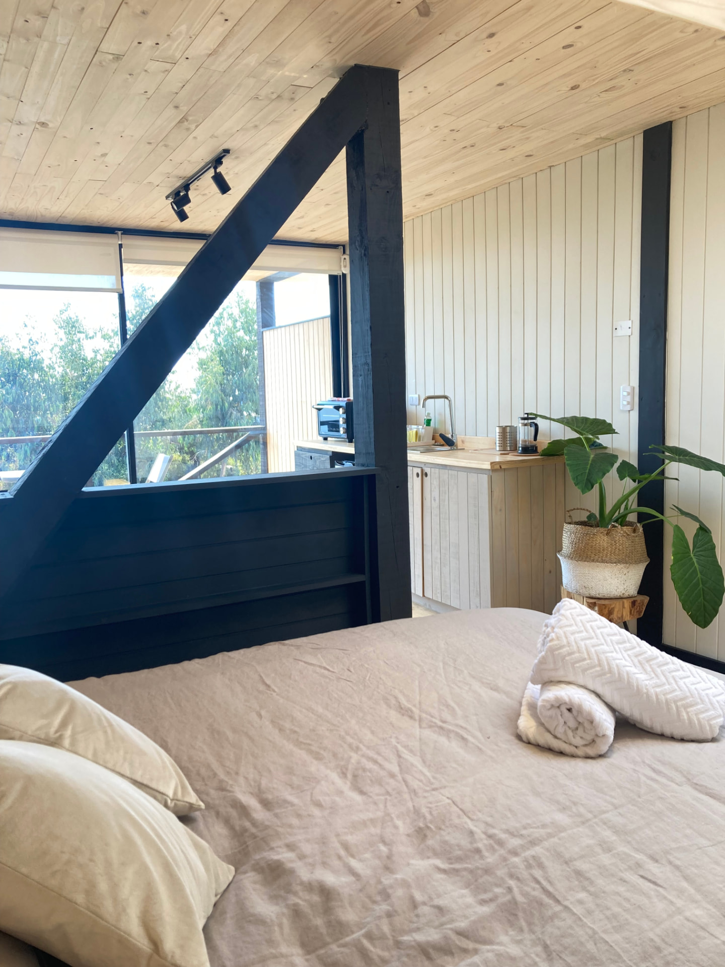 Interior de loft con vigas negras, cocina de madera y vista a los árboles